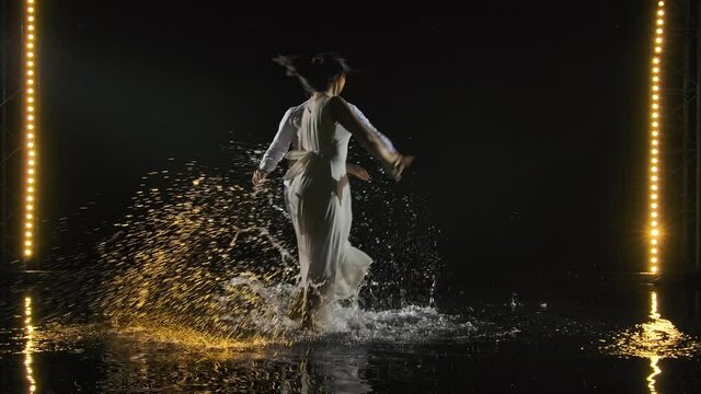 A man and a woman in white outfits are passionately dancing salsa and circling in dance. The couple dances on the surface of the water, creating many splashes. Slow motion.