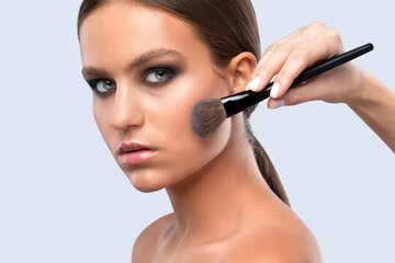 Portrait of a beautiful charming brunette teenage girl with beautiful fresh makeup and healthy clean skin.Makeup artist holds a powder brush in her hands. Professional makeup concept