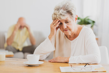 Senior woman with headache sitting at dining table drinking coffee