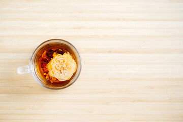 Black Chinese herbal tea with a flower inside the glass cup on the wooden background