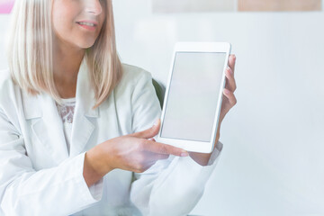 Pretty blonde nurse in medical uniform with tablet, copy space on empty white wall