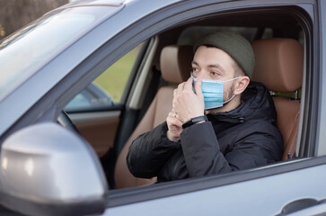 Male driver wearing mask in car during coronavirus outbreak.White bearded man wearing protective mask to avoid the infection of virus and polluted air spreading deseases inside of his car. 