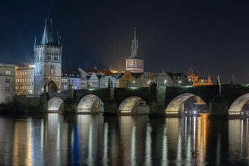 Fototapeta na wymiar illuminated Charles Bridge from 14 centuries and light from street lighting and stone sculptures on the bridge and light reflections on the surface of the Vltava river at night in Prague