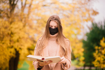 Young woman protecting from corona virus when walking in park. Autumn background.