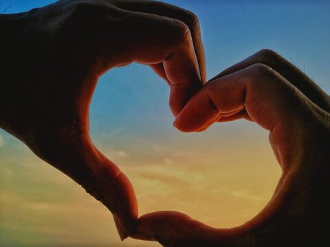 Close-up Of Hands Making Heart Shape Against Sky During Sunset