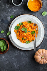 Pumpkin pasta with spinach in a white plate on a dark gray table. Dinner. Flat lay.