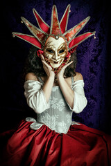 A young woman wearing a historical costume and a Venetian carnival mask