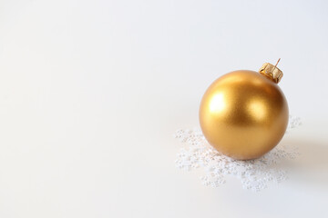 Background for Christmas time. Gold ball on a white background with snow confetti. Close-up. Isolated. Place for your design.