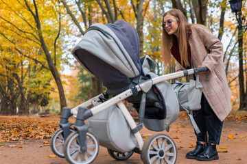 Fototapeta na wymiar Cheerful mom playing with newborn baby in stroller. Woman walking in the park with pram