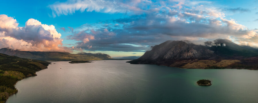Beautiful Panoramic View of Lake alongside Scenic Road surrounded by Mountains and Trees. Dramatic Sunrise Sky. Aerial Drone Shot. Taken near Klondike Highway, Southern Yukon, Canada.