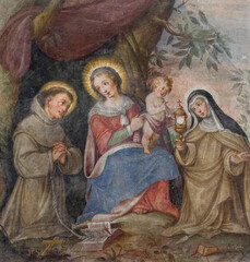 A fresco of the Virgin Mary with Infant Jesus among Saint Francis of Assisi and Saint Clare. The "Santa Maria del Carmine" church (Holy Mary of Carmel) in Pavia, Italy. Shot in 2017.