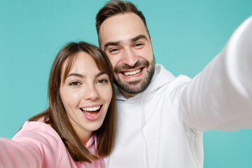 Obraz premium Close up of cheerful young couple two friends man woman 20s in white pink casual hoodie standing doing selfie shot on mobile phone isolated on blue turquoise colour wall background studio portrait.