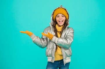 smiling stylish child presenting product, copy space. autumn season shopping. teenage girl in silver puffer jacket. trendy warm clothing. accessories shop for kid. enjoy weather on christmas holidays