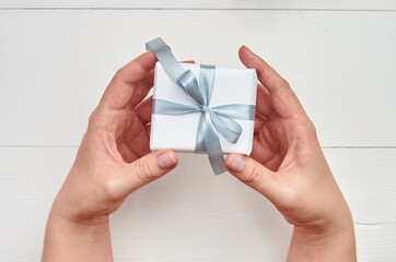 Female hands holding gift box over white wooden background
