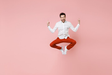 Fototapeta na wymiar Full length of crazy screaming young bearded man 20s wearing basic casual white shirt jumping depicting heavy metal rock sign horns up gesture isolated on pastel pink color background studio portrait.