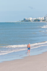back view, very far distance of a senior male walking on a tropical shoreline on sandy beach, on gulf of Mexico, on sunny day