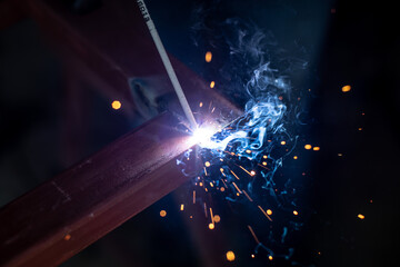 Young man with protective mask welding iron profile in a factory