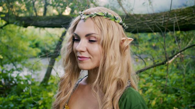 Portrait of young woman in cosplay elf clothes and with make-up on green background. Fantastic look, long blonde hair, forest crown. Halloween concept.
