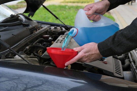 Driver or mechanic pouring windshield washer fluid to car