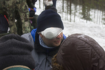 Training in first aid for eye injury. Reportage from a place in the winter forest where the exercises are taking place. Bandaging the victim's head