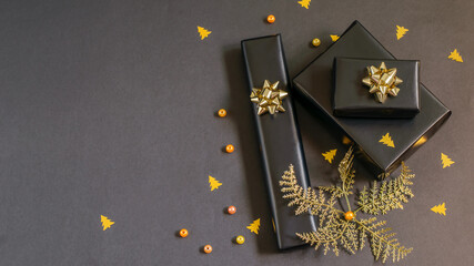 Fototapeta na wymiar Gift boxes wrapped in black festive paper with golden ribbon, fortuna gold colored bubles, beads and confetii. Christmas handmade gifts, diy concepts.