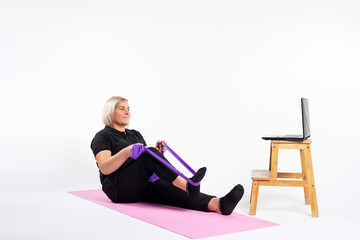 Senior woman sitting, doing exercises with an elastic band. Online training.