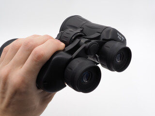 A man's hand holds a black tourist binoculars on a light background