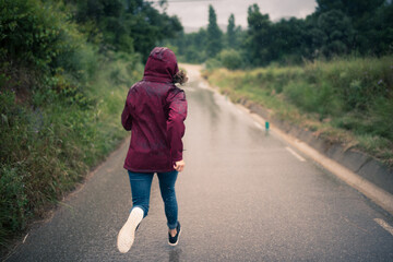 Girl in raincoat running down a rain-wet road.