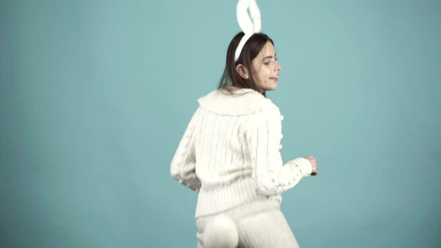 Funny model dressed in costume Easter bunny, standing on a blue background and sensually posing. Portrait of happy Easter bunny woman. Crazy girl celebrating easter.