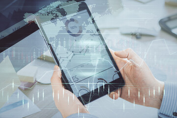 Double exposure of man's hands holding and using a phone and financial graph drawing. Analysis...