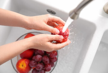 Woman washing fresh nectarine in kitchen sink, top view