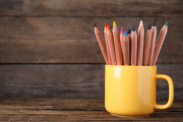 Obraz premium Colorful pencils in cup on wooden table. Space for text