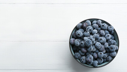 Tasty frozen blueberries in bowl on white wooden table, top view. Space for text