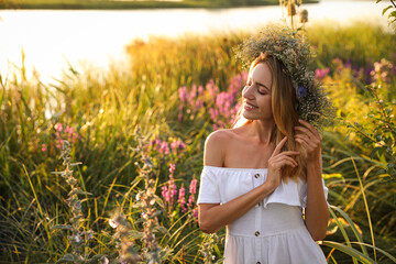 Young woman wearing wreath made of beautiful flowers outdoors on sunny day