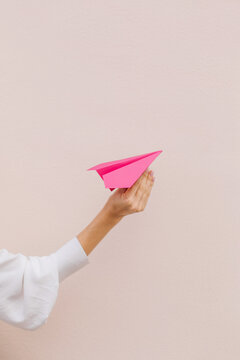 Women Hand Holding Pink Paper Airplane On Beige Background. Copy Space