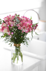 Fototapeta na wymiar Vase with beautiful alstroemeria flowers on countertop in kitchen. Interior design