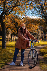 Girl cycling in public park, on the path between the trees with autumn colors