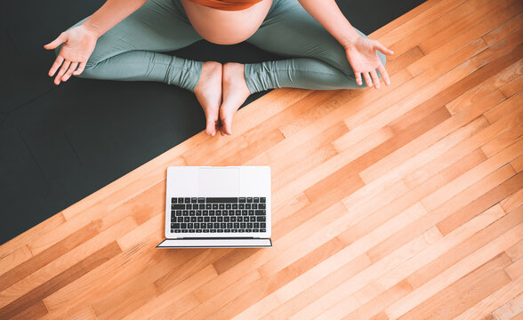 Closeup belly of pregnant woman practicing yoga online with laptop.