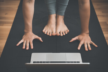 Closeup of female feet and palms on yoga mat with laptop.