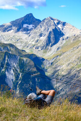 Hiker resting on grass near ski station Les deux Alpes and view on Alpine mountains peaks in summer, Isere, France