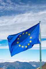 Blue with yellow stars Flag of Europe or European Union flag waving on mast in Alpine mountains in sunny day