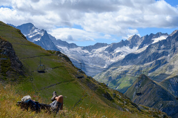 Hiker resting on grass near ski station Les deux Alpes and view on Alpine mountains peaks in...