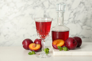 Delicious plum liquor, mint and ripe fruits on white table. Homemade strong alcoholic beverage