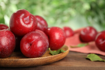 Delicious ripe plums on wooden table against blurred background, closeup. Space for text