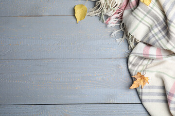 Fototapeta na wymiar Checkered plaid and dry leaves on light grey wooden table, flat lay. Space for text