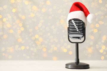 Retro microphone with Santa hat on table against blurred lights, space for text. Christmas music