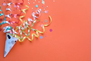Colorful confetti and streamers with party cracker on orange background, top view. Space for text - obrazy, fototapety, plakaty