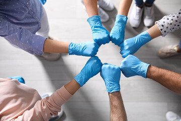 People in blue medical gloves joining fists indoors, top view
