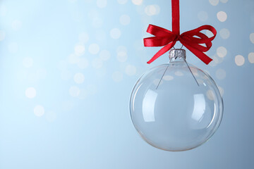 Transparent glass Christmas ball against light background with festive lights. Space for text