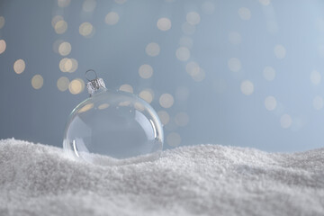 Transparent Christmas ball on snow against blurred fairy lights, space for text